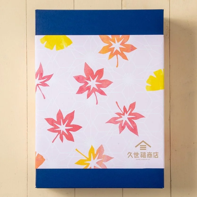 青い上下と白い中央部に紅葉とイチョウの葉がデザインされた、久世福商店のギフトボックス