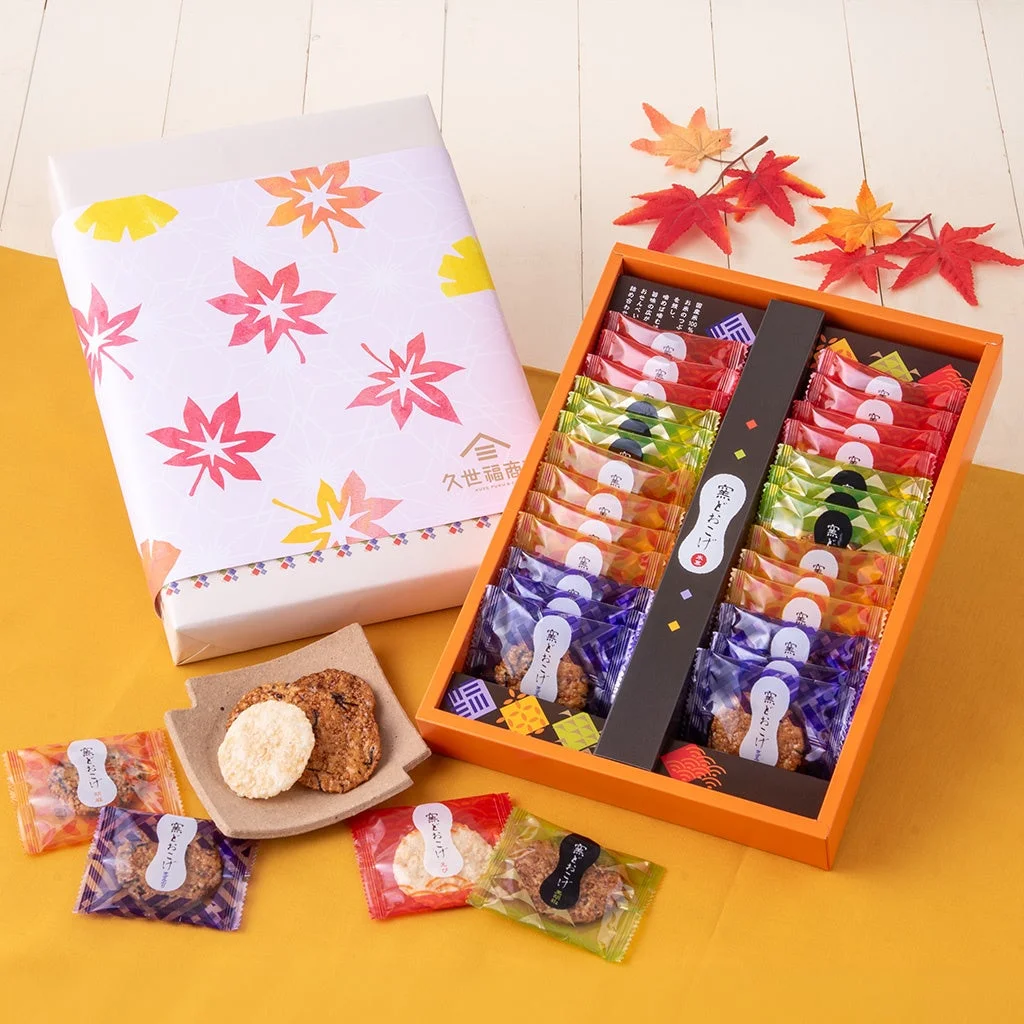 秋の紅葉をモチーフにした包装紙のギフトボックスと、中身の「蜜とろおこげ」が多数個包装で並べられた箱