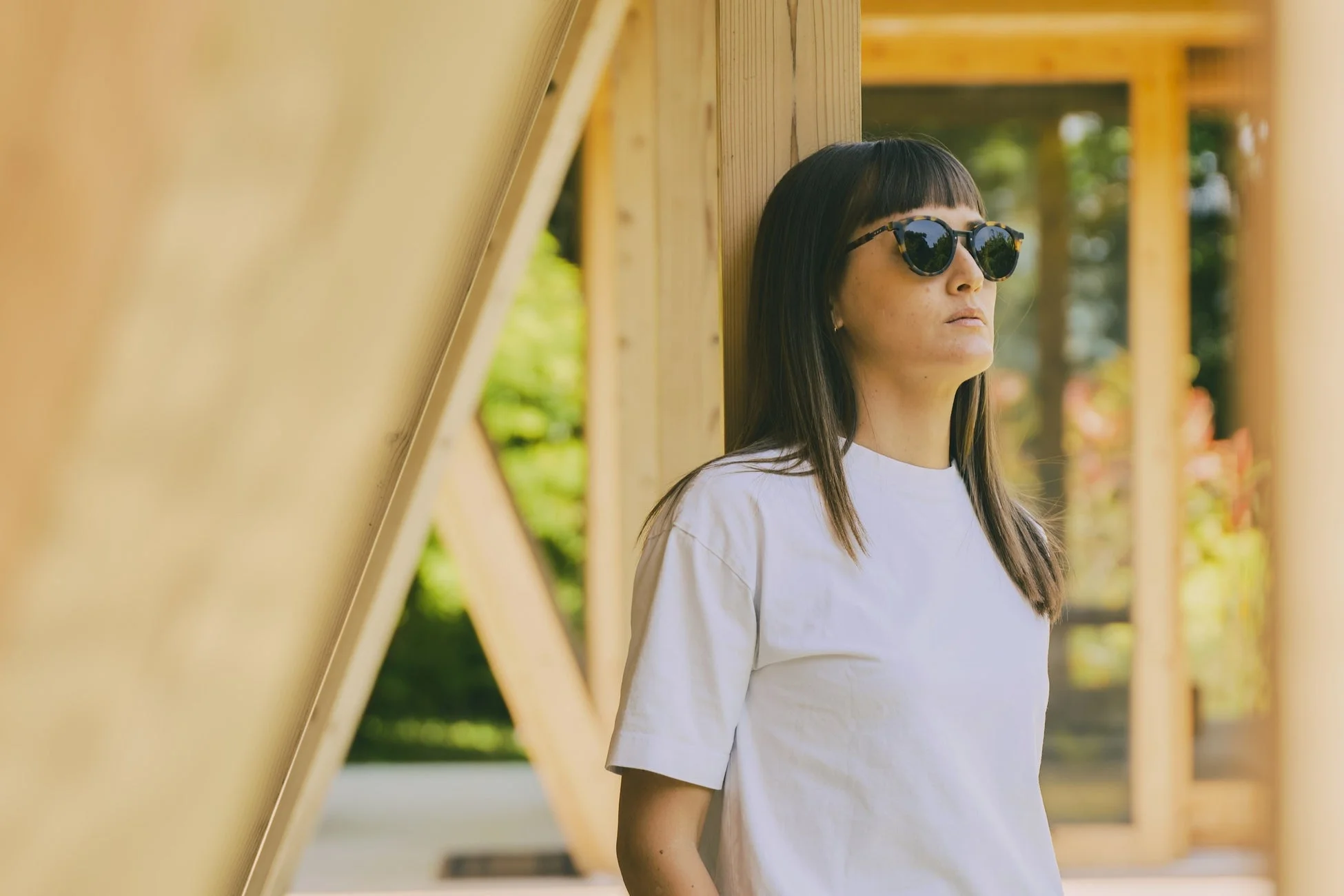 サングラスと白いTシャツを着た女性が屋外の木製の構造物に寄りかかっている